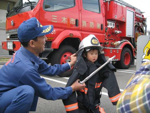 消防団のおじさんに防火衣を着せてもらい記念撮影の画像